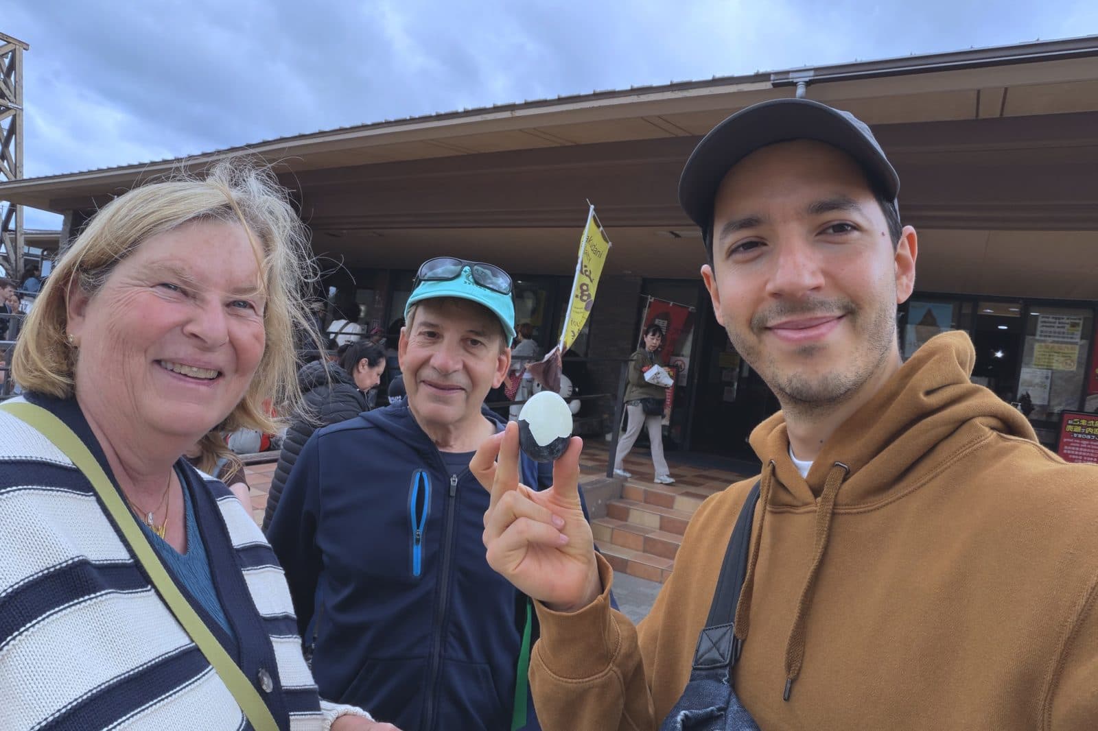 the founder and two guests outside the rest house at Owakudani, one of Hakone's black eggs held up to the camera