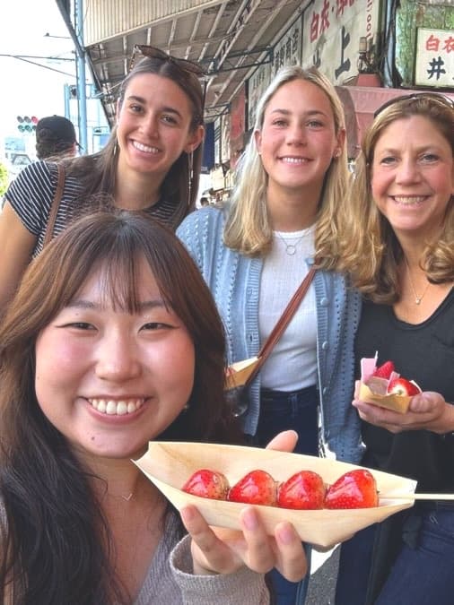 a guide and three guests with a boat of candied strawberries on a market street