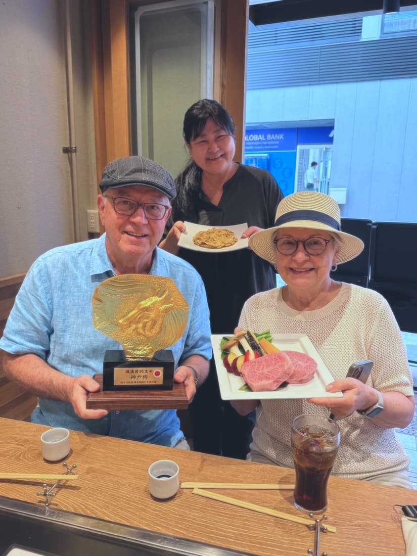 two guests holding a golden plaque and a plate of wagyu, their guide behind with another dish