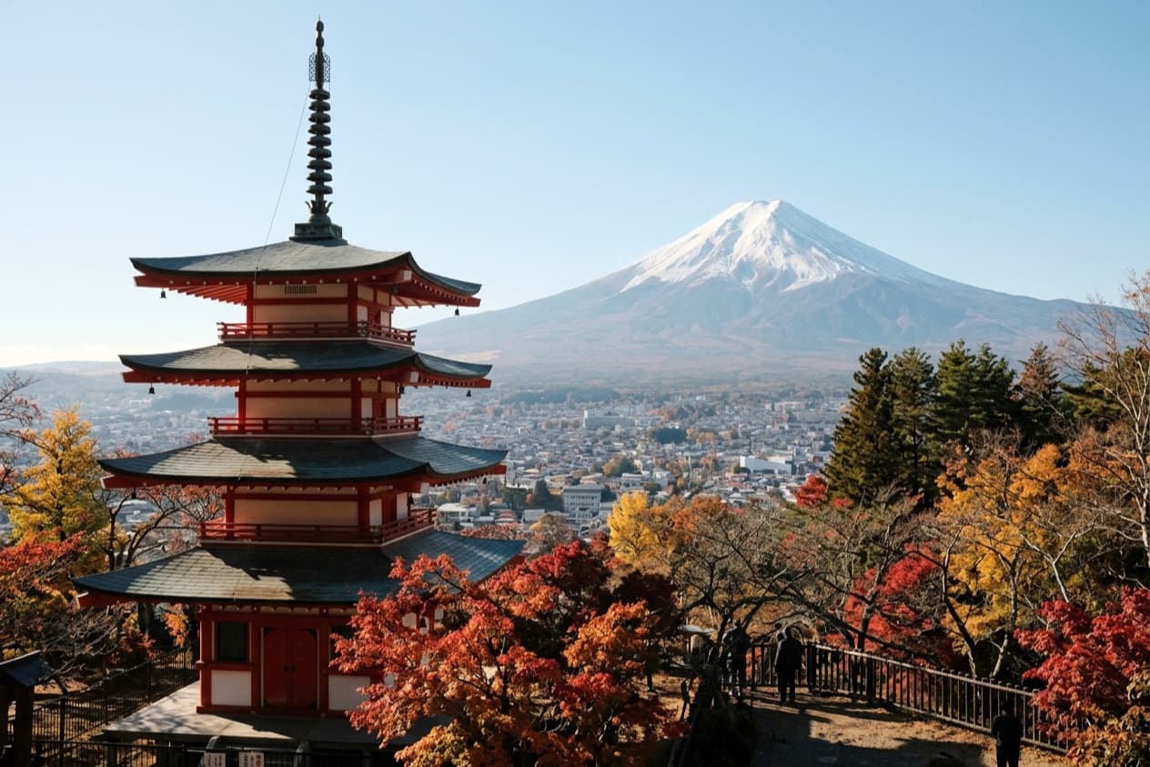 the five-storey Chureito pagoda on its hillside above Fujiyoshida, autumn maples around it and snow-capped Mount Fuji across the valley
