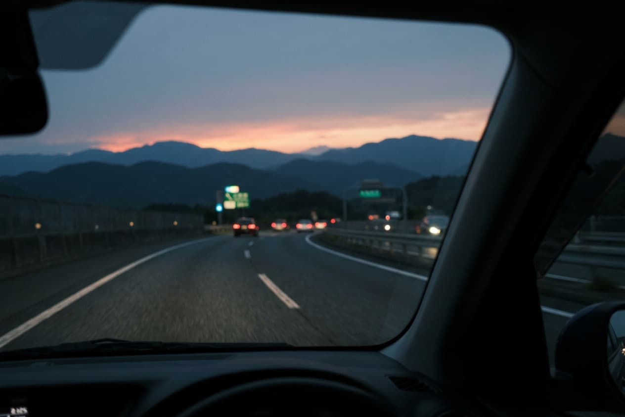 the road home at dusk seen from inside the car, tail-lights ahead and the hills going blue under the last light