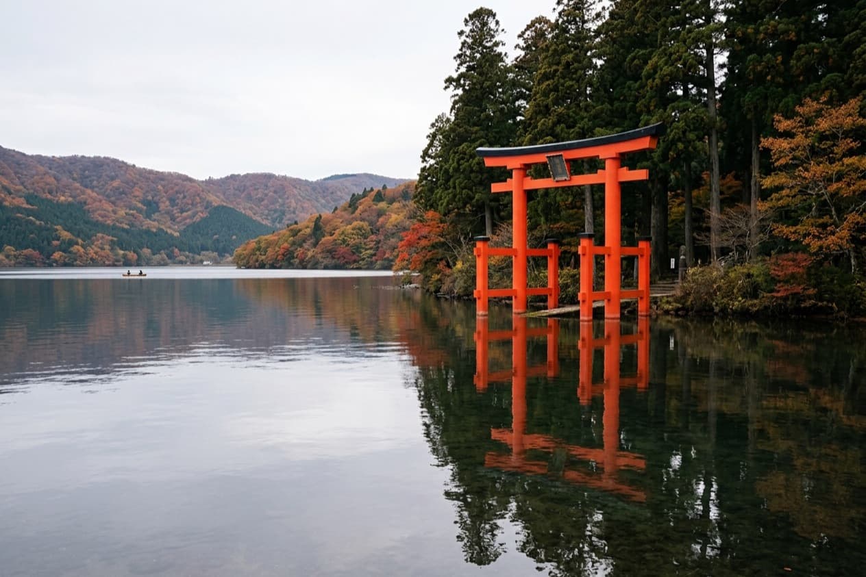 the vermilion torii of Hakone Shrine standing in Lake Ashi, cedars behind it and the gate doubled in still water