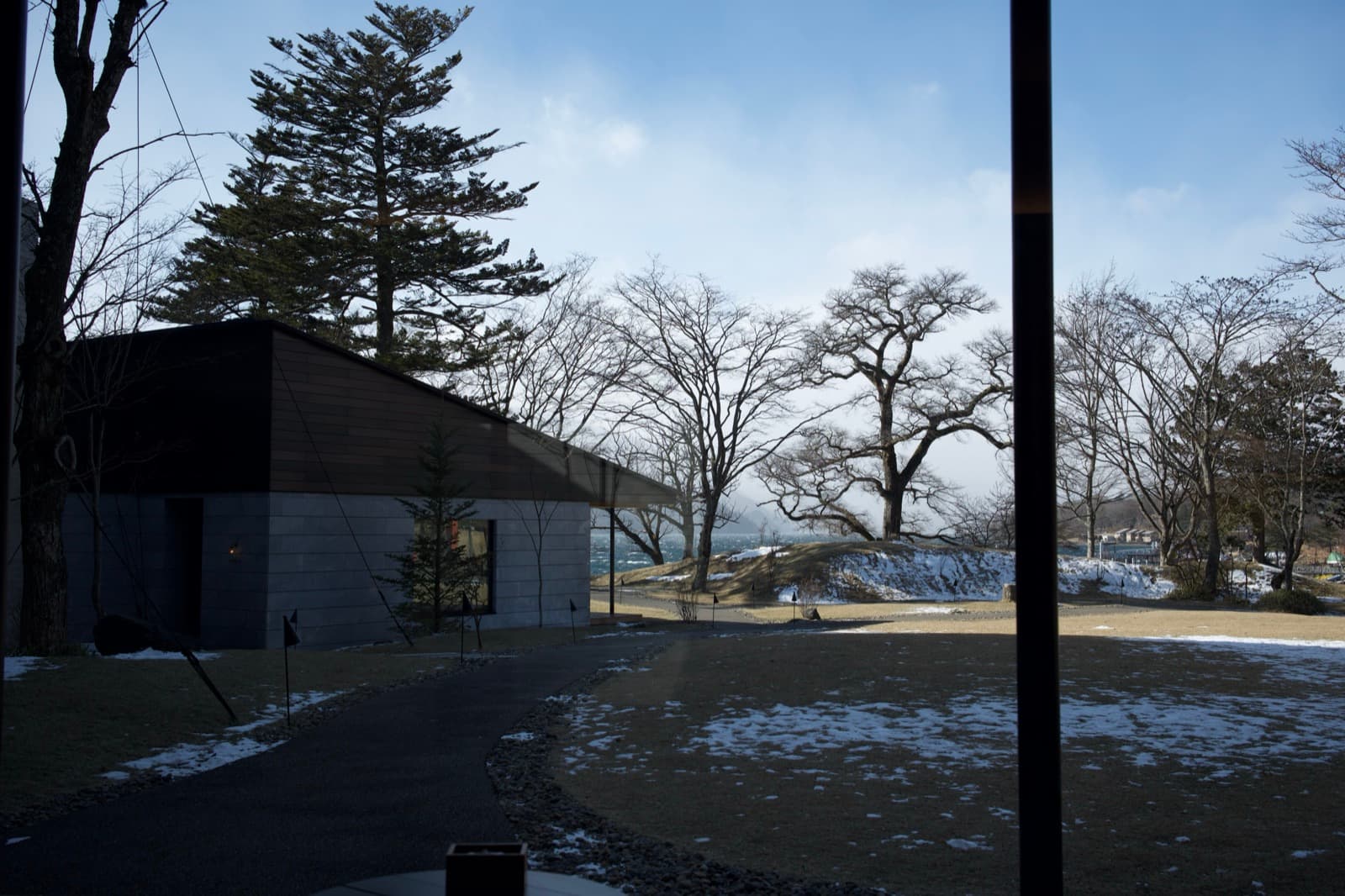 Lake Chuzenji and wind-bent trees seen through a dark-framed window, snow on the ground